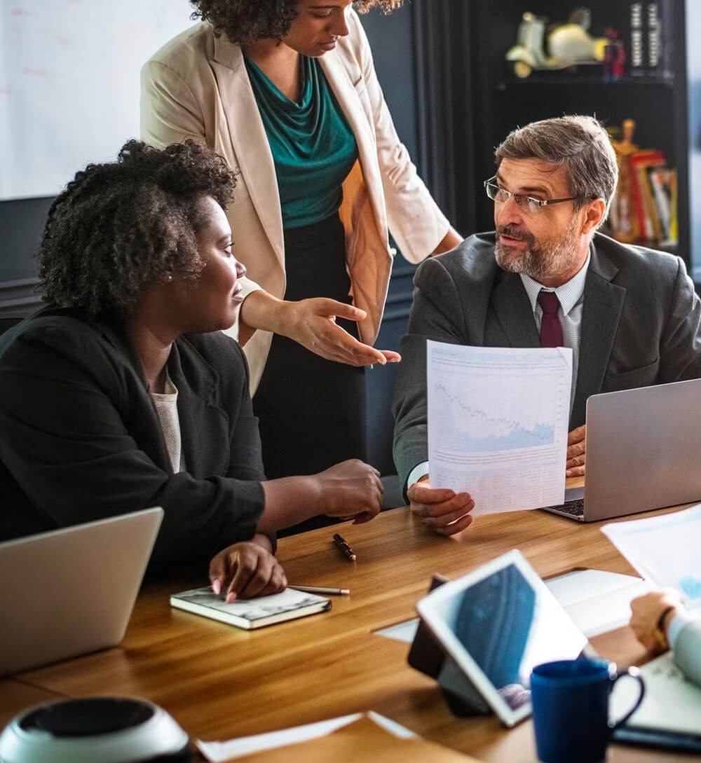 a group of people talking with each other in a meeting room on a working desk