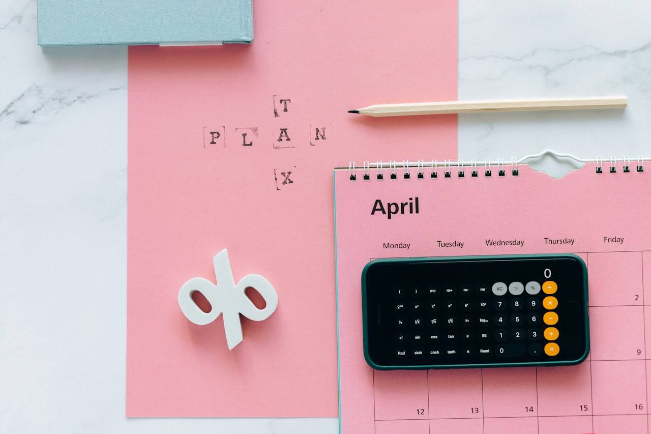 A phone with an opened calculator app, a pencil, and a 3d percentage sign placed on a pink sheet of paper showcasing solid taxation services